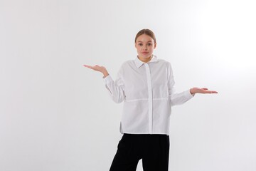 Young woman in a white shirt gestures with open hands in a neutral setting while conveying...