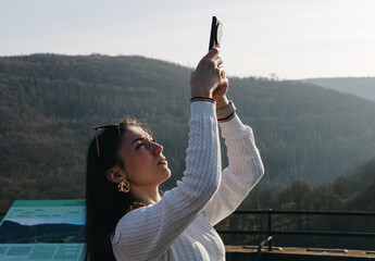 A girl takes a photo of the landscape on her smartphone from an observation deck.