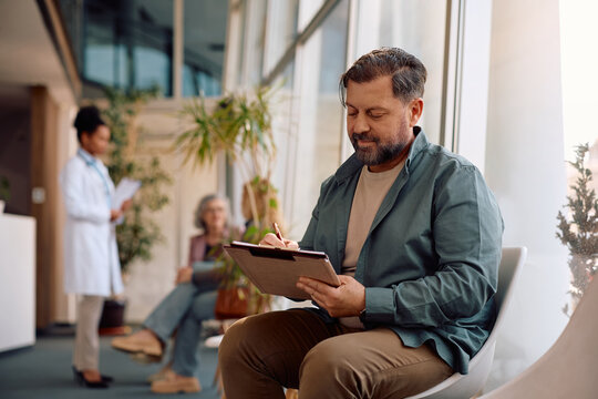 Mature man filling out paperwork before doctor's appointment at medical clinic.