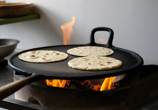 Three tortillas cooking on a hot comal placed over a wood fire in a restaurant kitchen