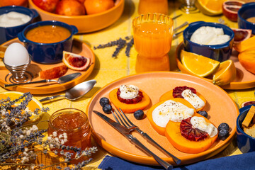 Sliced persimmon with ricotta, blood orange and honey, completing a colorful breakfast table setting