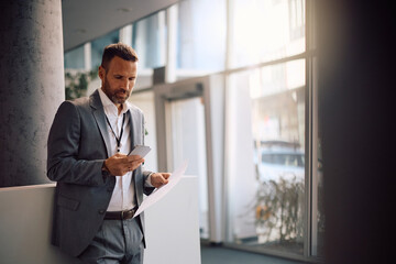 Fototapeta premium Businessman using cell phone while analyzing reports in office.