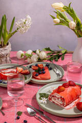 Pink strawberry dessert crepes and rolls with spring flowers decorating the table