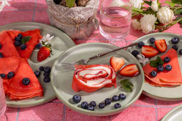 Red pancakes, rolled crepe with cream cheese filling and fresh berries for a festive breakfast