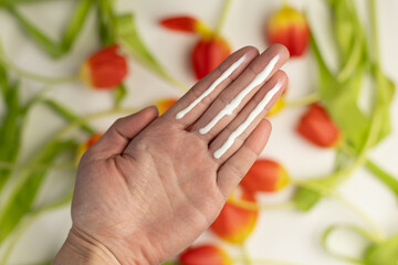 A person applying the correct amount of sunscreen for the face and neck – three finger lengths, with tulips in the background. Concept of applying sunscreen in spring. 
