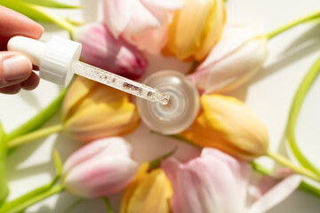 Closeup of dropper with serum surrounded by tulips. Concept of spring skincare.