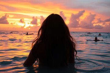 Silhouette of woman in water, vibrant sunset sky, orange and pink clouds, ocean horizon, surfers in distance, dramatic lighting, atmospheric scene, golden hour, serene mood, back view, long hair, 