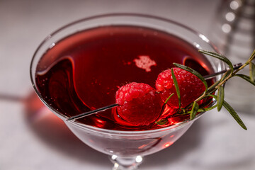 Red cocktail with raspberries and rosemary in a martini glass