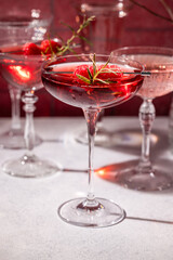Elegant coupe glasses with red cocktails and fresh raspberries garnished with rosemary sprig