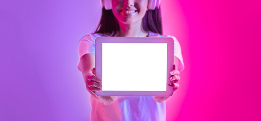 A smiling young woman wearing headphones holds a blank tablet in front of her against a vibrant...