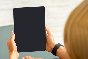Group workout online. Coach woman with fitness tracker looking in digital tablet with blank screen, sitting on mat on floor with bottle of water, close up, copy space