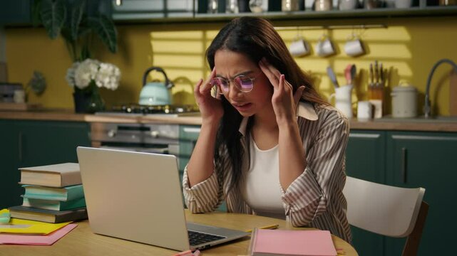 Arabian businesswoman work online laptop at home kitchen girl tired exhausted student freelancer suffer headache stress overwhelmed Indian woman massaging head pain studying computer overwork migraine