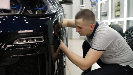 Engineer checks car in auto service. Car repair and detailing, worker checks struts on front wheel.