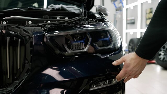 Mechanic inspecting front bumper and headlight of modern car in auto repair shop