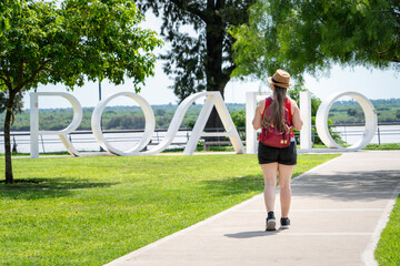 Mujer turista recurriendo los parques verdes de la Ciudad de Rosario. Caminata frente a cartel de...