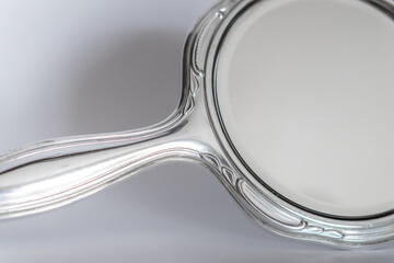 An antique hand mirror featuring a ornate silver handle and a round reflective surface. The mirror...