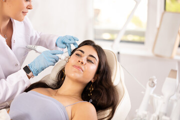 Young brunette girl having facial beauty massage with beauty machine attachment