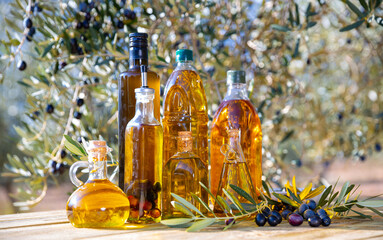 Bottles with olive oil and olive branch on a wooden table on a background of nature