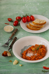 Traditional Italian Tomato Soup with Bread - Pappa al Pomodoro on green background, cutlery, slices of bread, bunch of tomatoes, typical  homemade Tuscan dish, tasty, appetizing tomato soup, close-up.