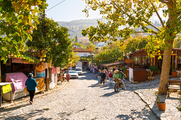 Tourists walk down a cobbled hillside street past shops and markets in the touristic center of the ancient village of Sirince, Turkey.