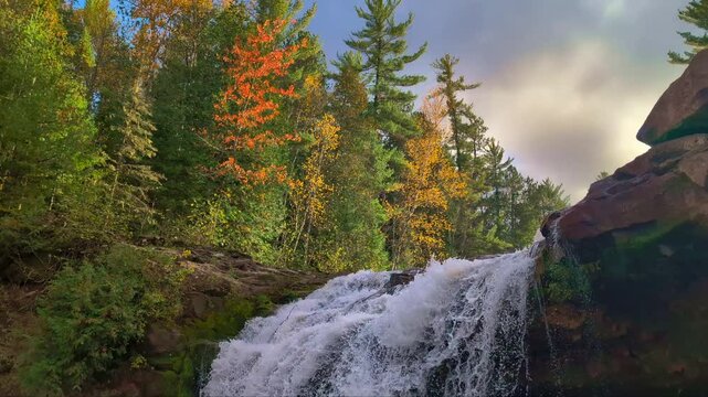 Evening sunlight illuminates autumn foliage over O Kun de Kun Falls in Michigan