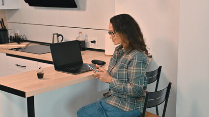 Woman Working Remotely from Home with Laptop and Smartphone in Kitchen
