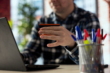Credit card used by man in apartment filling out online forms on laptop for loan, closeup. Focus on card used by person in blurry background typing on notebook, completing loan application forms