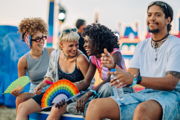 Friends enjoying music festival with rainbow fans and refreshments