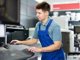 Workman in uniform operating computerised machne to mix paint