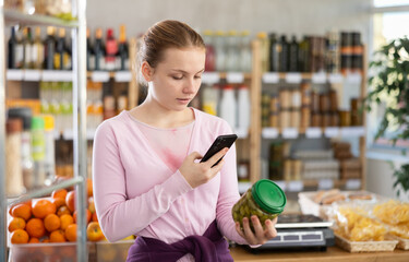 Checking expiration date of chips - female shopper scans QR code on label of jar canned olives using her smartphone