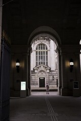 Fototapeta premium A solitary woman in a light-colored coat stands beneath a grand historic archway, leading to an ornate building with classical architecture. Berlin, Germany
