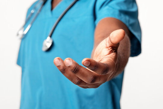 A man doctor in scrubs extends his hand in a welcoming gesture, showcasing a commitment to patient care in a healthcare setting, cropped