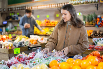 Attentive young girl choosing onions in plastic bag in large vegetable market