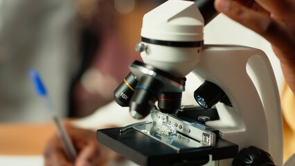 University student prepares for exam by researching cells and microorganisms under the microscope. Using books and papers from the academic database in the college library. Close up. Camera B.