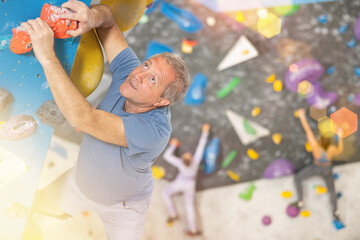 Adult man in sportswear practicing rock climbing on climbing wall