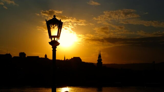 Sunset illuminating a city skyline with a warm glow. Sunset casts a warm glow behind a city skyline, creating a striking silhouette of a lamppost against the backdrop of urban architecture
