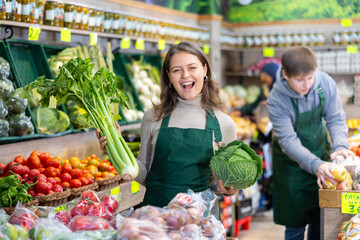Positive girl seller with cabbage in her hands in the grocery department of the supermarket