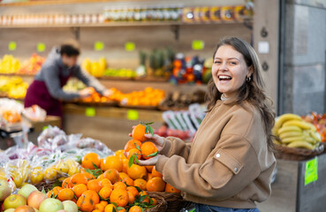Happy young girl chooses and buys ripe delicious tangerines in grocery section of the supermarket