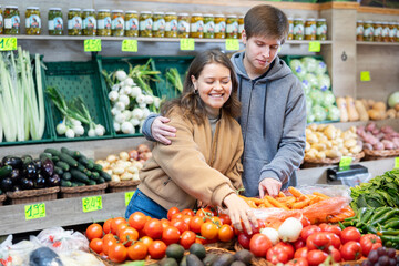 Happy young couple buying together tomatoes in large fruit and vegetable market