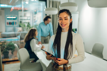 Smiling businesswoman holding tablet with colleagues working in background