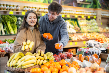 Couple of young woman and young guy choose tangerines and bananas in vegetable shop