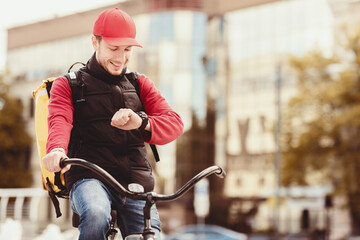 Happy Courier Checking Time On Wristwatch Delivering Food On-Time Sitting On Bike In City. Delivery Concept. Free Space For Text