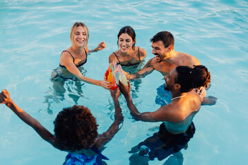 Happy friends are toasting colorful drinks in swimming pool