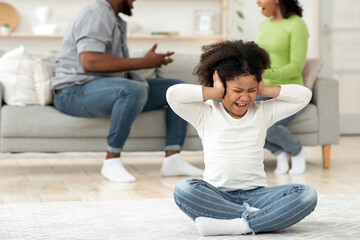 Fototapeta premium A young black child sits on the floor, covering her ears in distress while her parents argue in the background. The atmosphere is tense in their cozy living room.