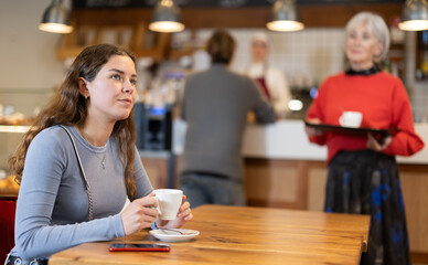 Food court girl visitor sits near table, drinks coffee and spends time in public place. Bored client spend time at cafe hall