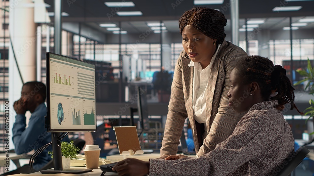 Poster female employee and manager gathered around a workstation discussing objectives and strategizing sol