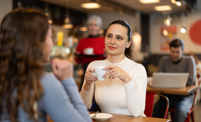 Two friends meeting in cafe. Woman talks to her friend over a cup of coffee