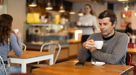 Cafe visitor drinks coffee alone. Man whiles away time and waits for meeting in chain cafe, spend time while drinking coffee.