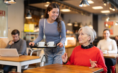 Adult daughter takes care of elderly mother in cafe - brought tray with two cups of coffee