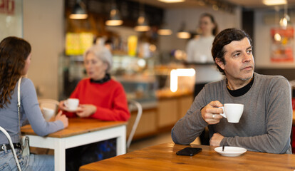 Lonely man drinking coffee and looking at mobile phone screen. Waiting for meeting
